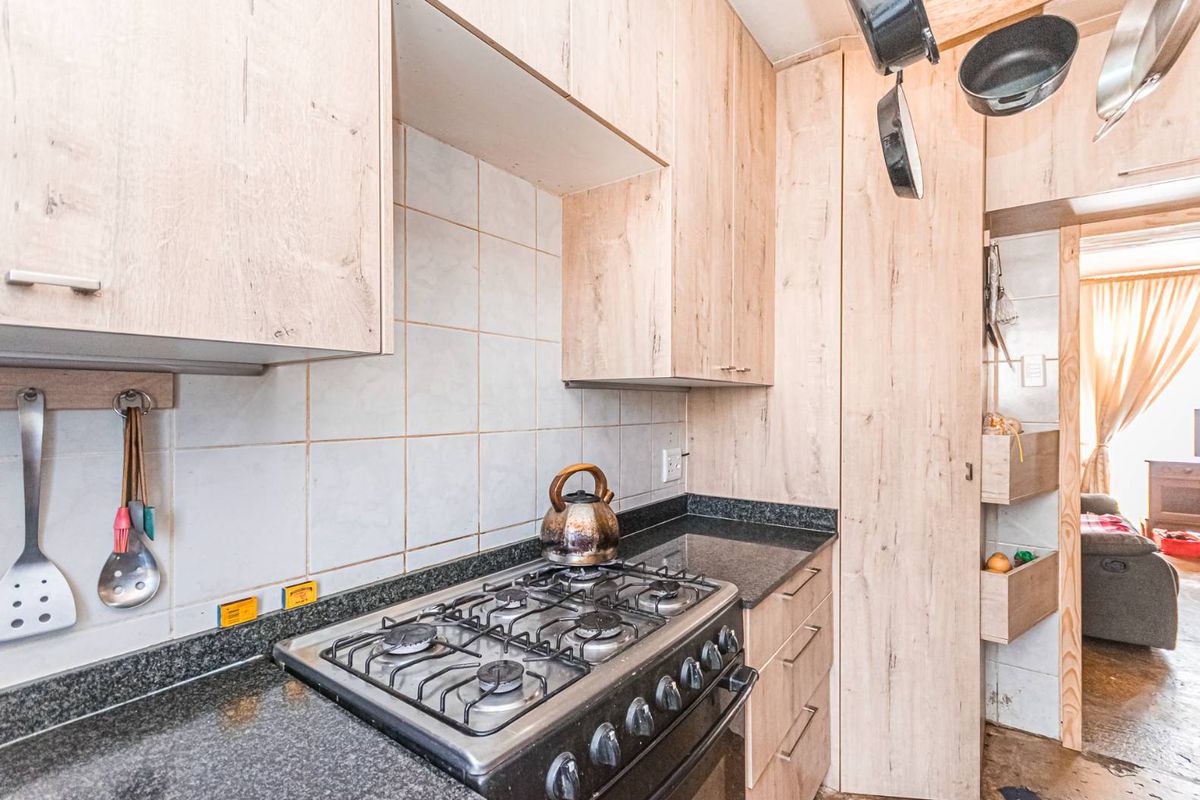 A functional kitchen featuring light wood-look cabinetry, granite countertops, a gas stove, and a built-in pantry cupboard with tiled backsplash.