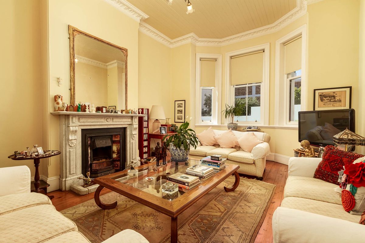A character-filled living room featuring an ornate marble fireplace, classic bay windows, and original timber flooring with decorative ceiling detailing.