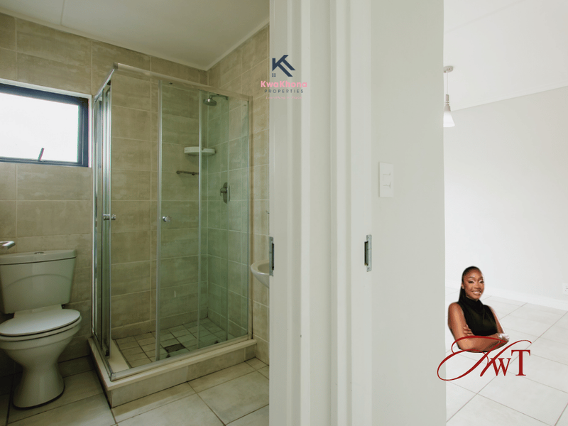 A clean, modern bathroom featuring a glass-enclosed shower, tiled walls, and floor, adjacent to an open-plan living area.