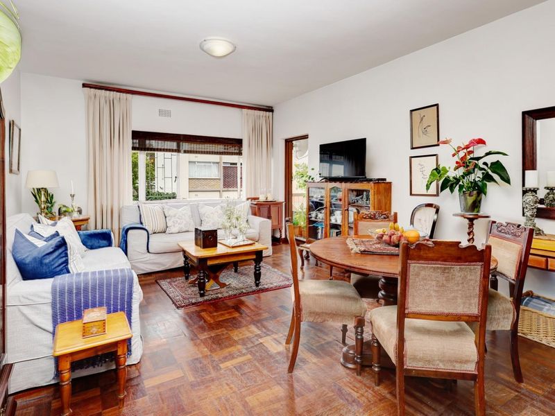 Open-plan living and dining area featuring classic parquet flooring, neutral walls, and access to an outdoor space through a sliding door.