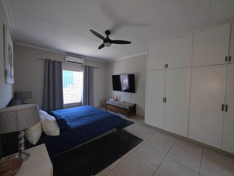 A well-maintained bedroom featuring built-in cupboards, a ceiling fan, and a split-system air conditioner, finished with neutral floor tiles.