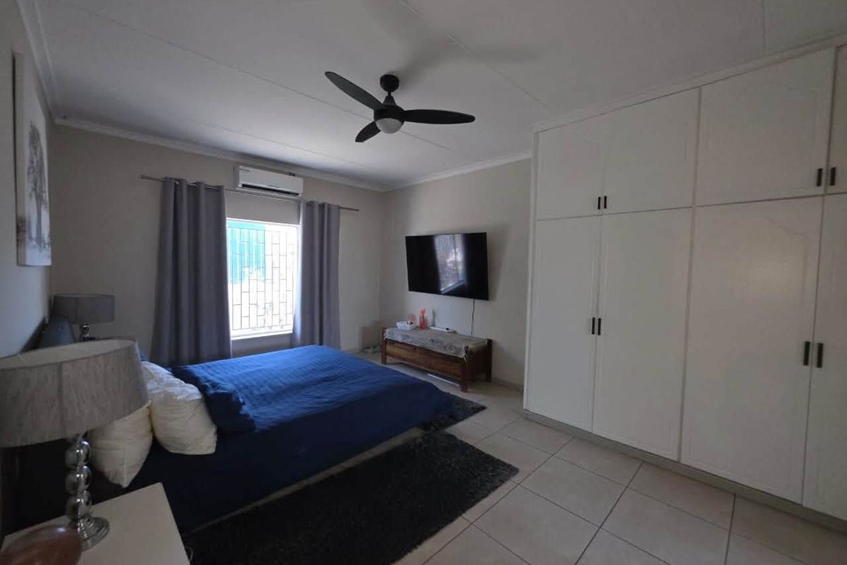 A well-maintained bedroom featuring built-in cupboards, a ceiling fan, and a split-system air conditioner, finished with neutral floor tiles.