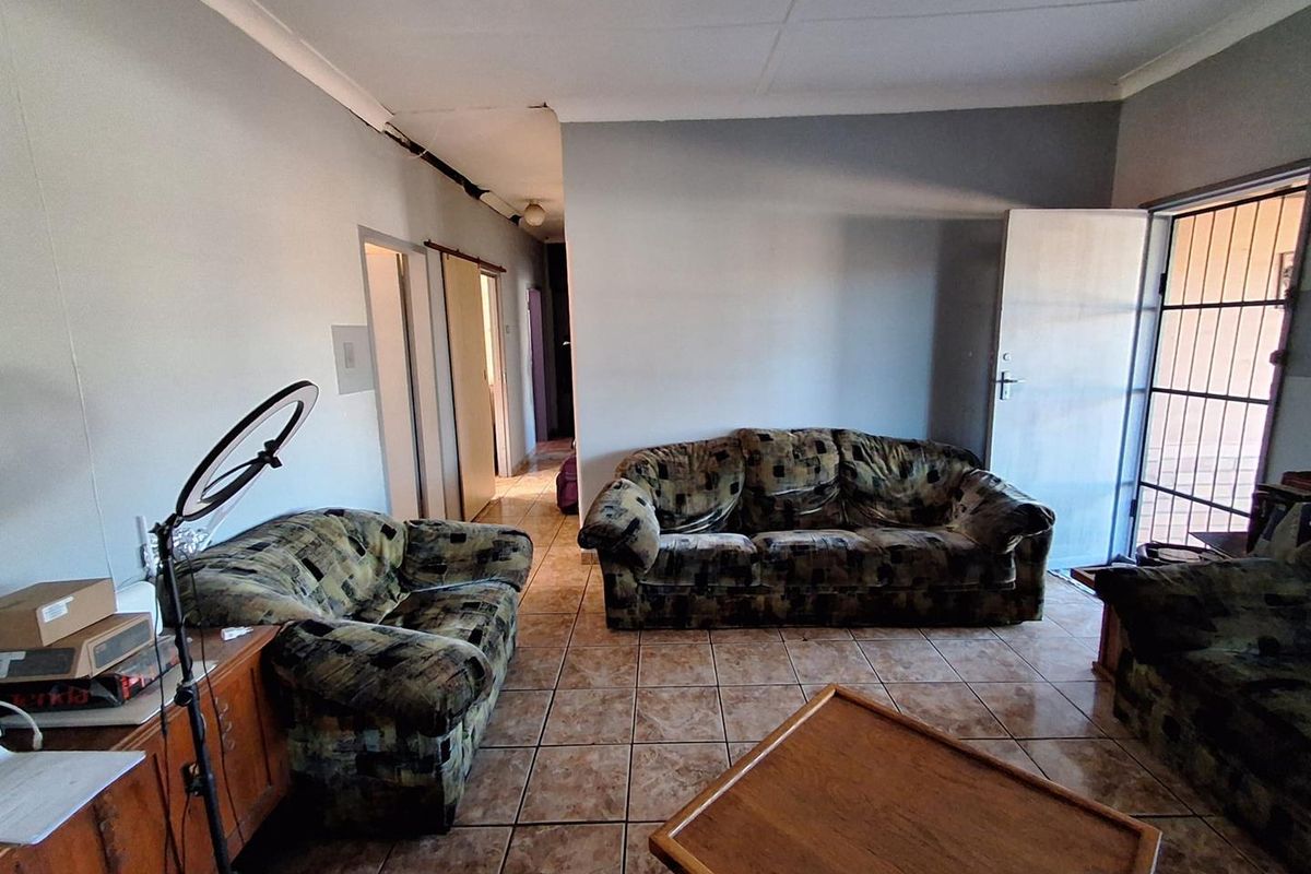 A living room featuring ceramic floor tiles, a security gate, and visible wear to the ceiling and wall finishes.