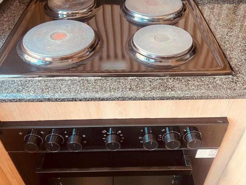 A close-up view of a built-in electric oven and hob set into a granite countertop with decorative slatted wood wall paneling.