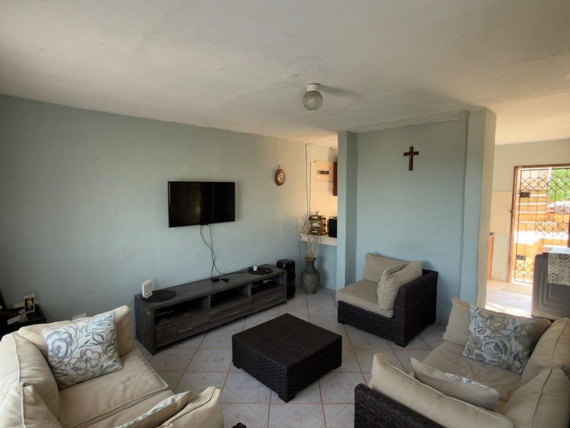A living room area featuring tiled flooring and a pass-through window connecting to the kitchen space.
