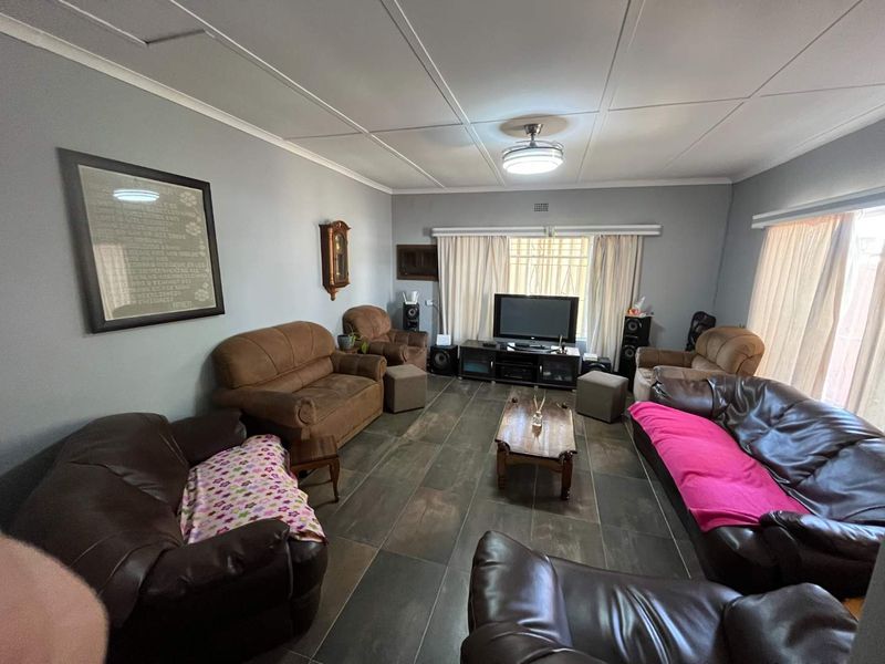 A spacious living room featuring dark tiled flooring, a ceiling fan, and large windows with security bars, offering a functional and comfortable living space.