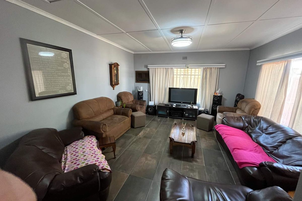 A spacious living room featuring dark tiled flooring, a ceiling fan, and large windows with security bars, offering a functional and comfortable living space.