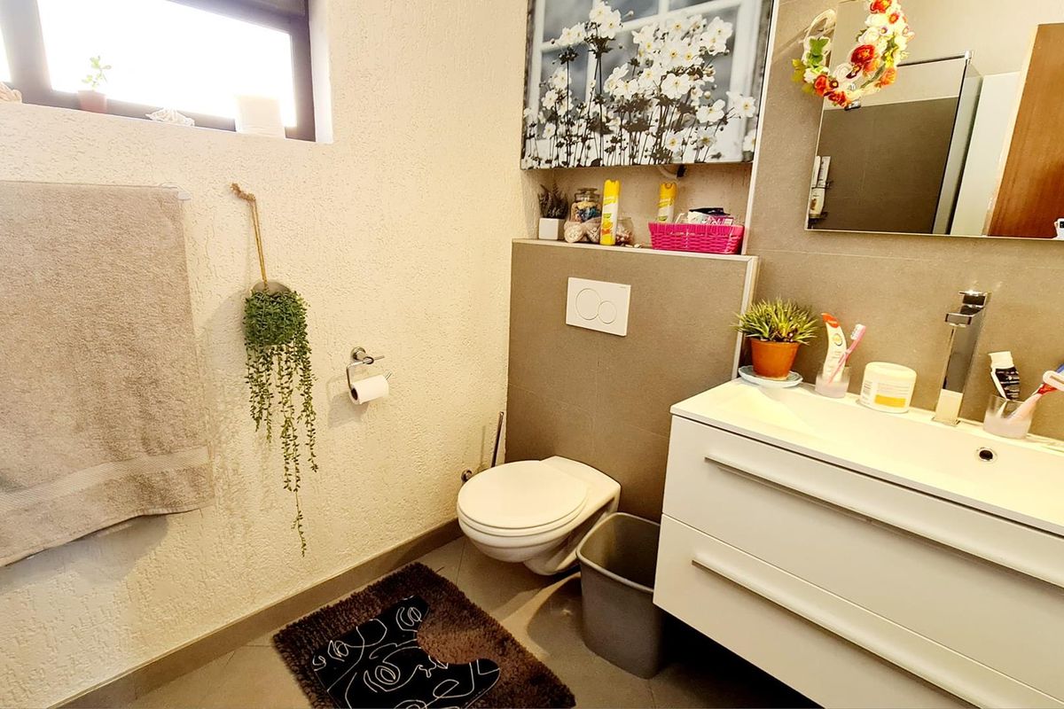 A modern bathroom featuring a wall-mounted toilet, a sleek vanity with an integrated basin, and neutral-toned wall tiling.