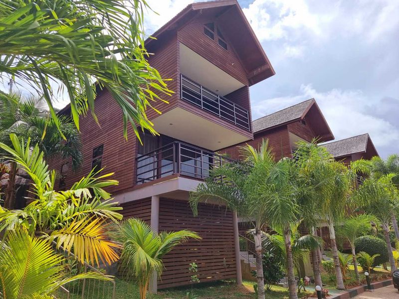 A multi-level commercial property featuring timber-clad facades, private balconies with metal railings, and landscaped tropical surroundings.