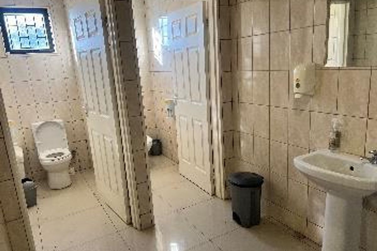 A functional industrial restroom facility featuring multiple toilet cubicles, pedestal washbasins, and fully tiled wall and floor surfaces.