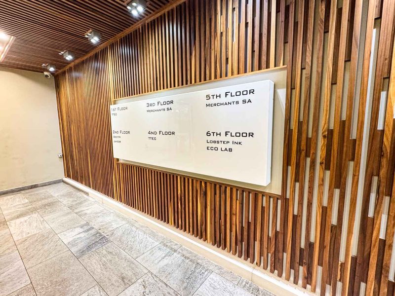 Modern building entrance lobby featuring high-quality slatted timber wall paneling, stone flooring, and a clear tenant directory signage board.