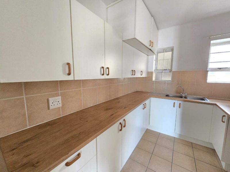 A functional kitchen featuring white cabinetry, wood-look laminate countertops, tiled backsplash, and tiled flooring with ample natural light.