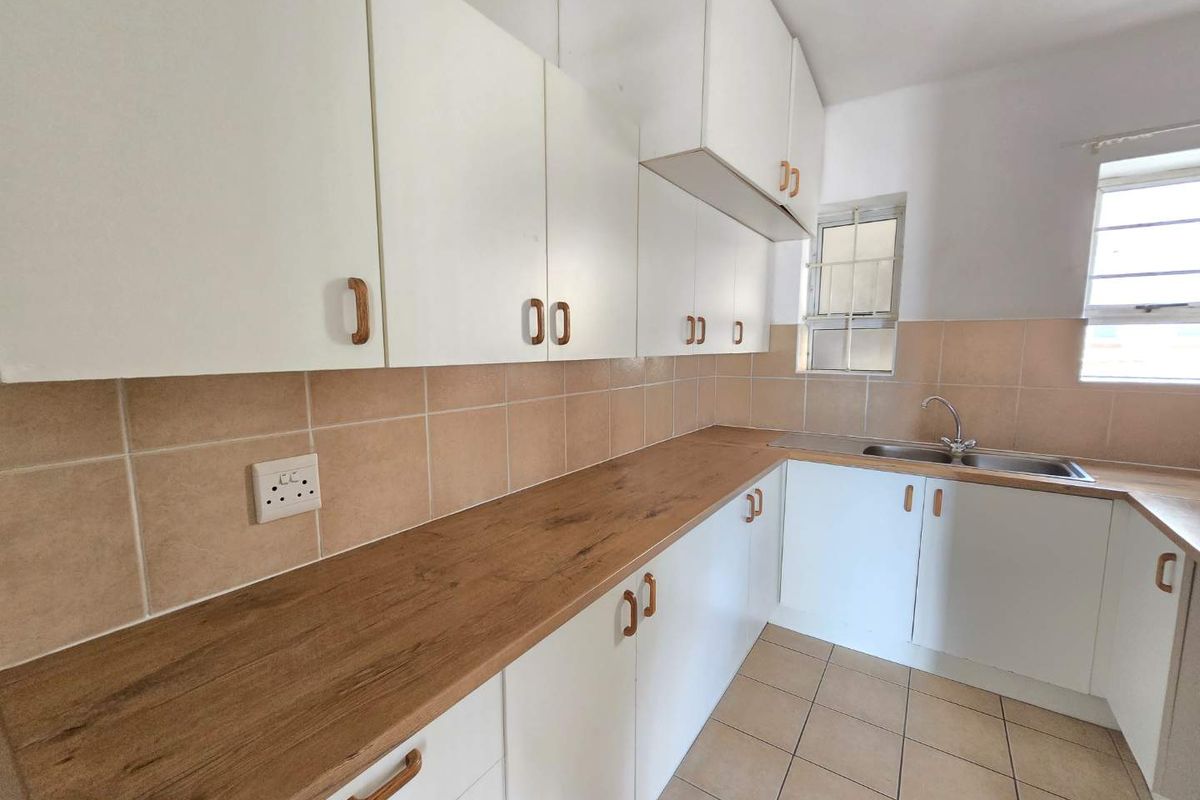 A functional kitchen featuring white cabinetry, wood-look laminate countertops, tiled backsplash, and tiled flooring with ample natural light.