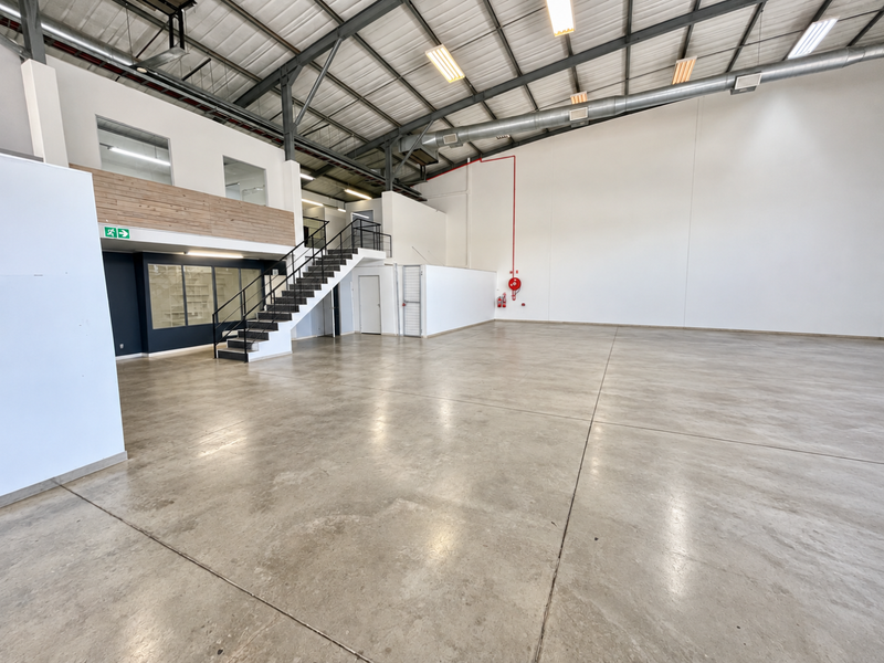 Spacious open-plan industrial unit featuring high ceilings, polished concrete floors, a mezzanine level with staircase, and integrated fire safety equipment.