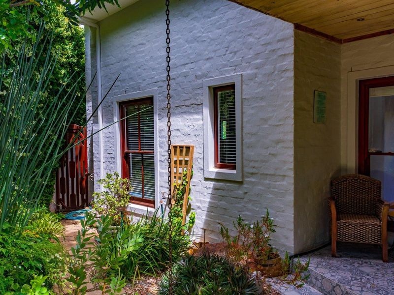 A charming rear exterior view featuring a painted brick facade, timber-framed windows, and a covered patio area with patterned tiling and a rain chain.