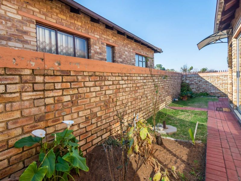 A private rear garden area featuring a brick boundary wall, paved walkway, and established garden beds adjacent to the townhouse structure.