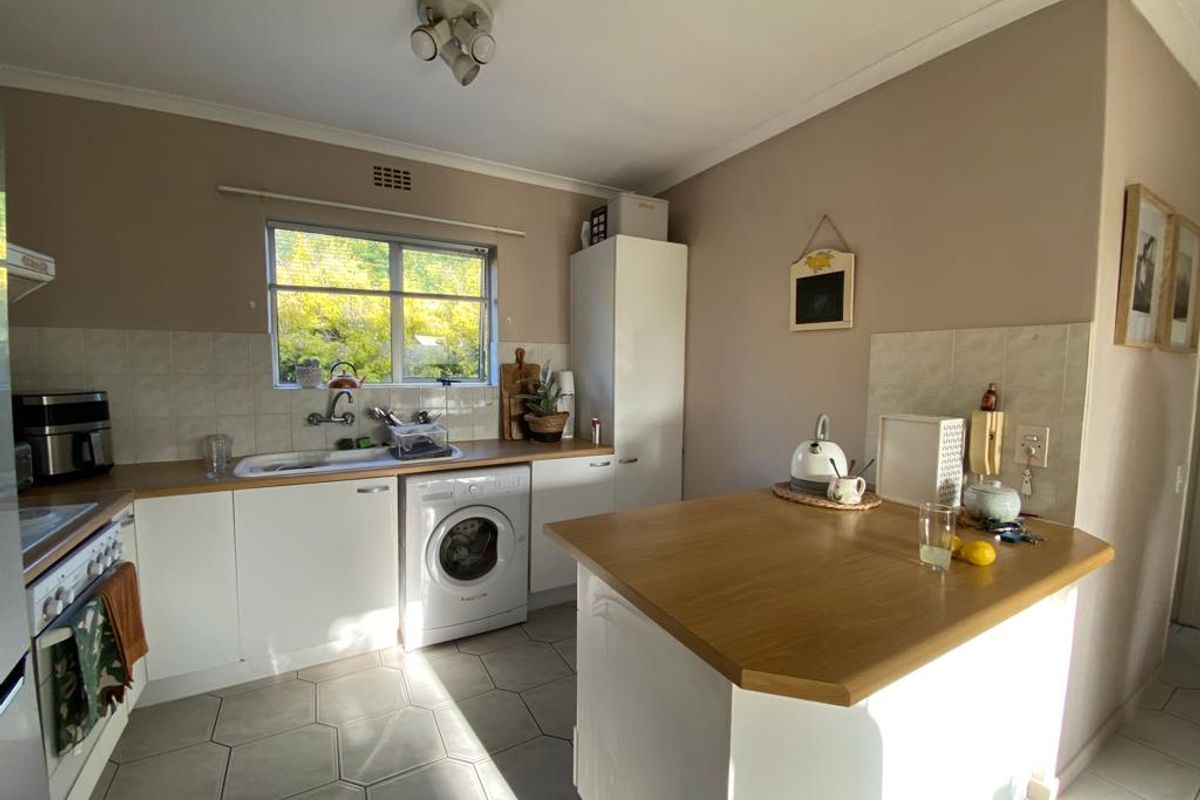 Functional kitchen featuring white cabinetry, wood-look laminate countertops, a built-in breakfast bar, and tiled flooring with a convenient integrated laundry space.
