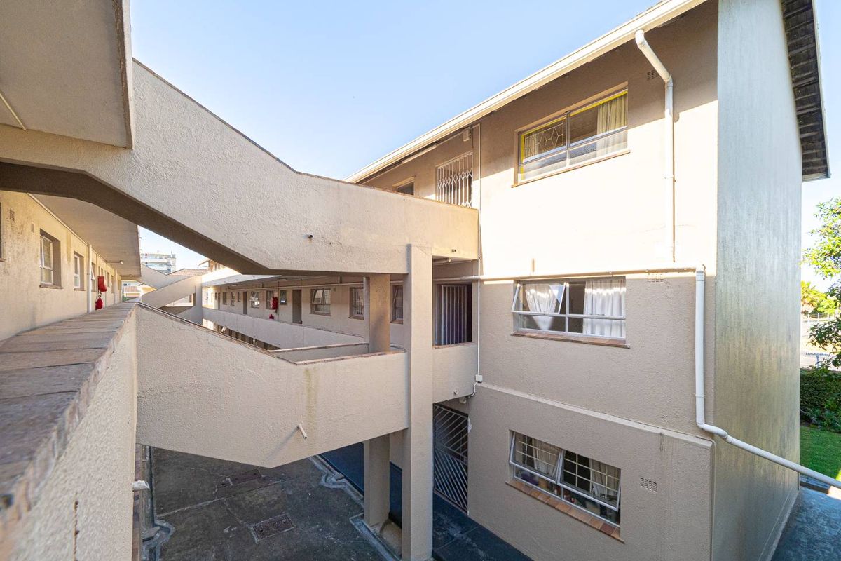 Exterior view of an apartment complex featuring concrete walkways, staircases, and multi-level residential units with security gates and windows.