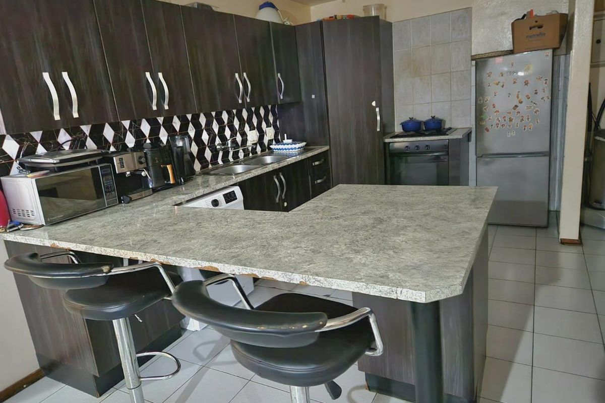 Kitchen featuring dark wood-look cabinetry, a breakfast bar with laminate countertop, tiled backsplash, and built-in oven and hob.
