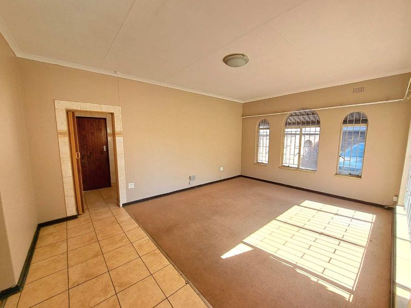 An empty living room featuring a combination of tiled and carpeted flooring, arched windows with security bars, and neutral wall finishes.