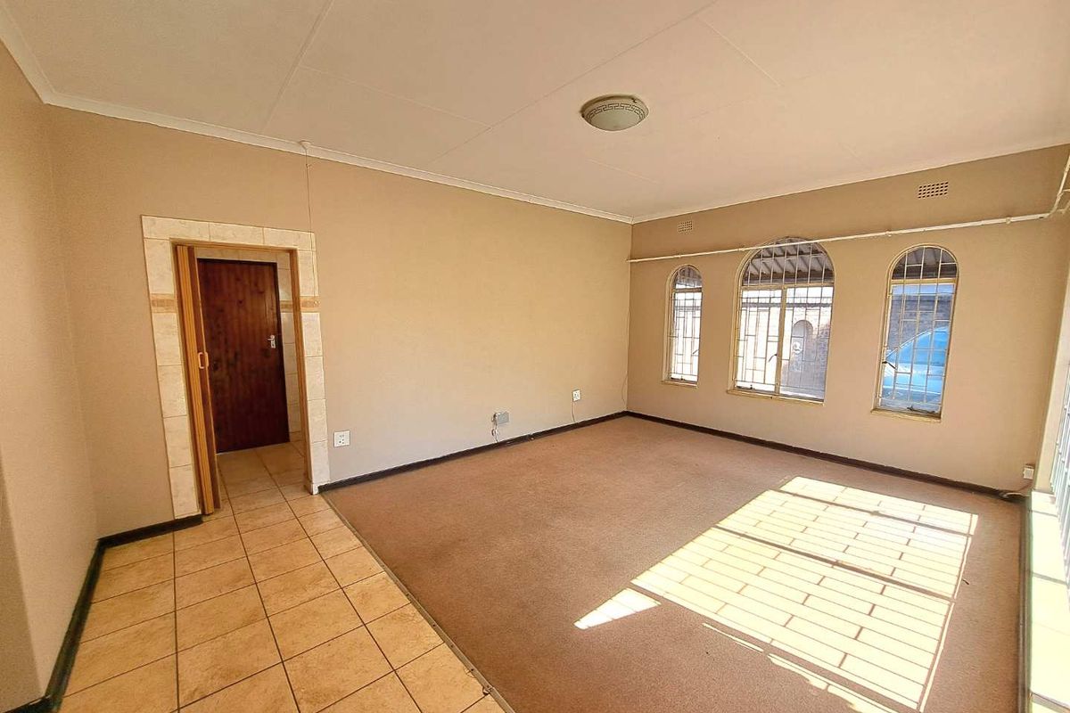An empty living room featuring a combination of tiled and carpeted flooring, arched windows with security bars, and neutral wall finishes.