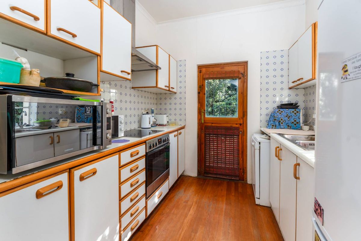 A functional galley-style kitchen featuring white cabinetry with timber trim, tiled splashbacks, built-in oven, and direct access to the rear exterior.