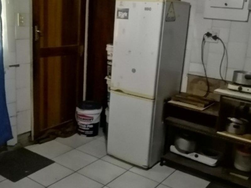 A functional scullery or utility area featuring tiled flooring, wall-mounted electrical distribution board, and direct access via a wooden door.