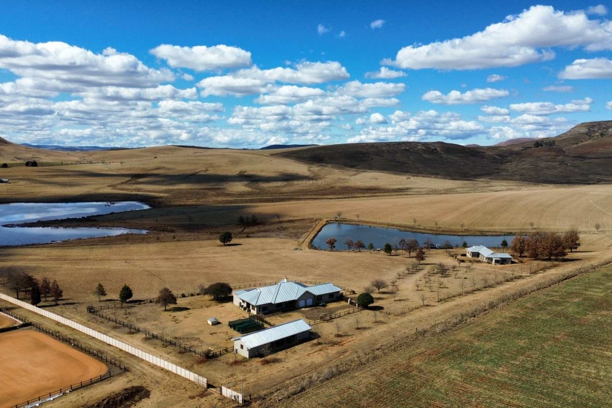Aerial view of a rural farm property featuring multiple buildings, fenced paddocks, and private dams set against a scenic landscape.