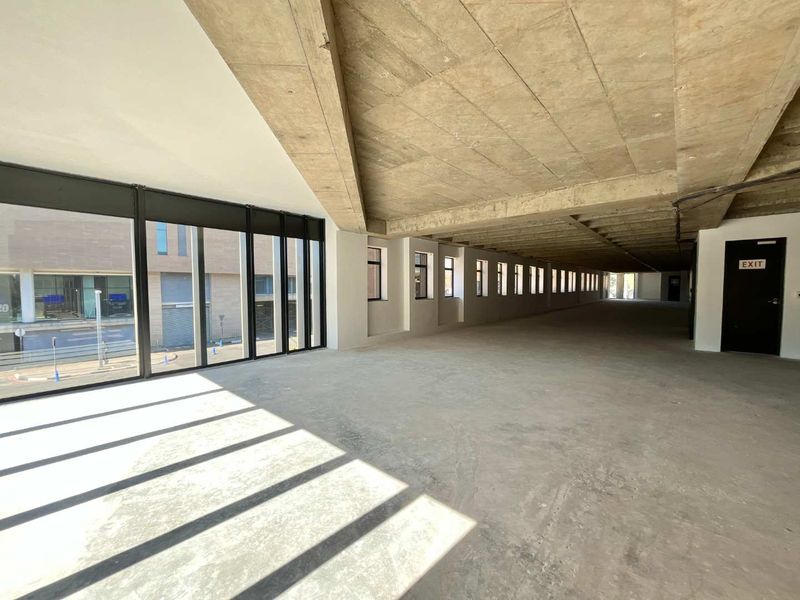 A spacious, open-plan office shell featuring exposed concrete ceilings, large windows providing ample natural light, and a concrete floor finish.