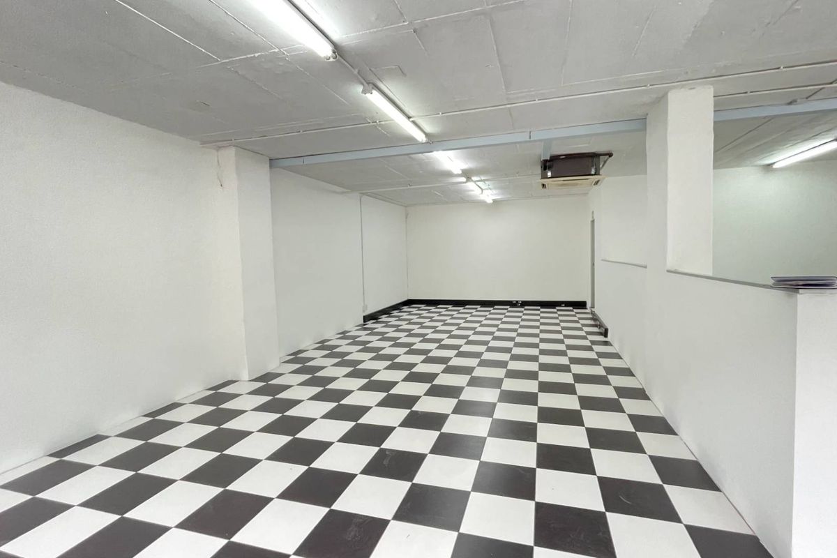 An open-plan retail space featuring checkered flooring, white walls, structural columns, and ceiling-mounted air conditioning, providing a versatile blank canvas for business operations.