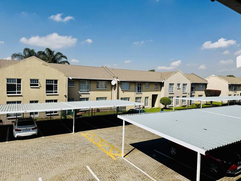 Exterior view of an apartment complex featuring paved parking areas with covered carports and well-maintained communal grounds.