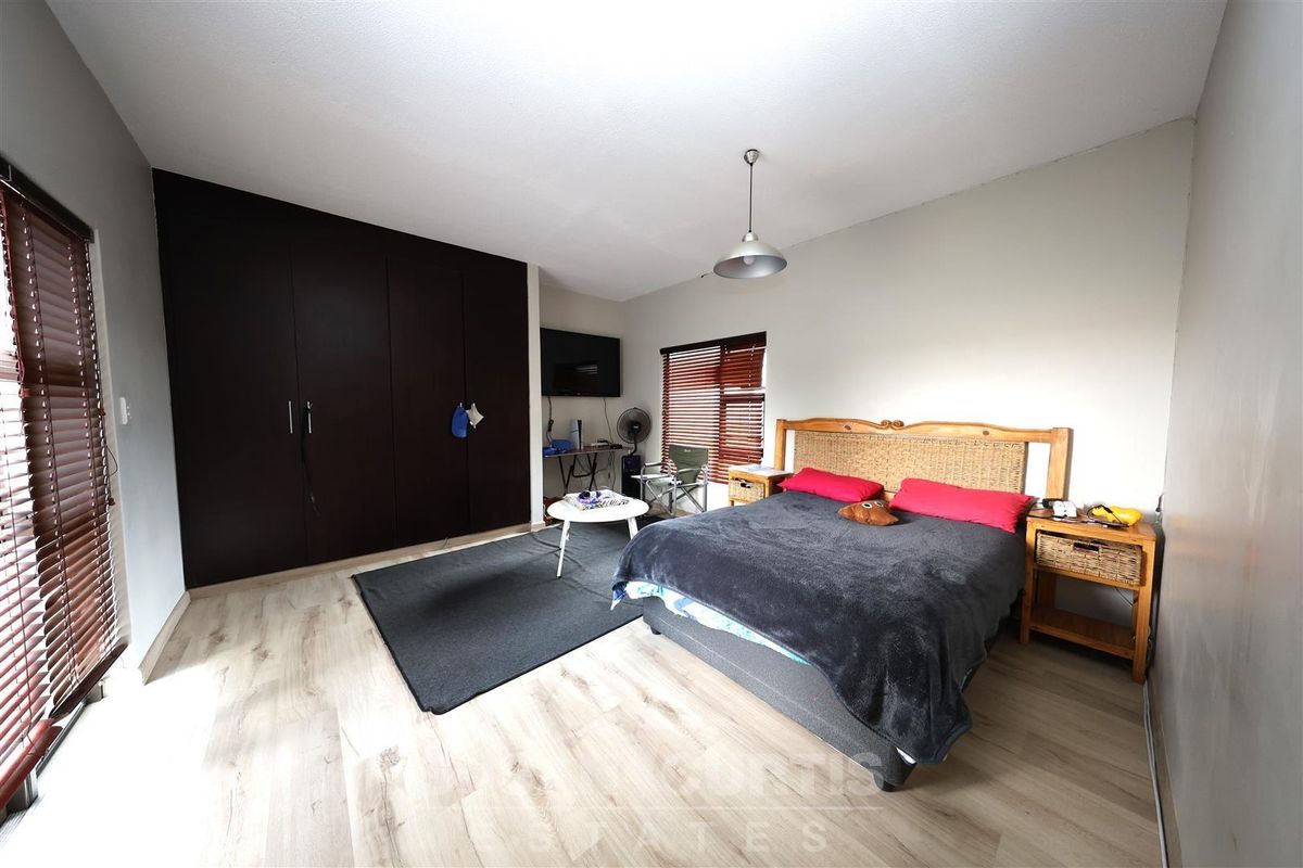 A spacious bedroom featuring light wood-look flooring, dark built-in cupboards, and venetian blinds.