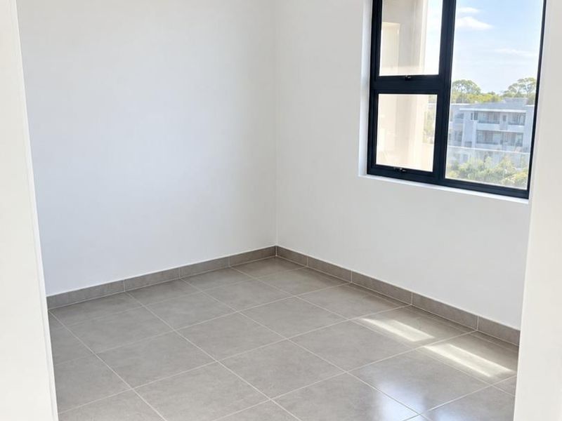 A bright, empty bedroom featuring neutral floor tiles and a modern black-framed window with natural light.