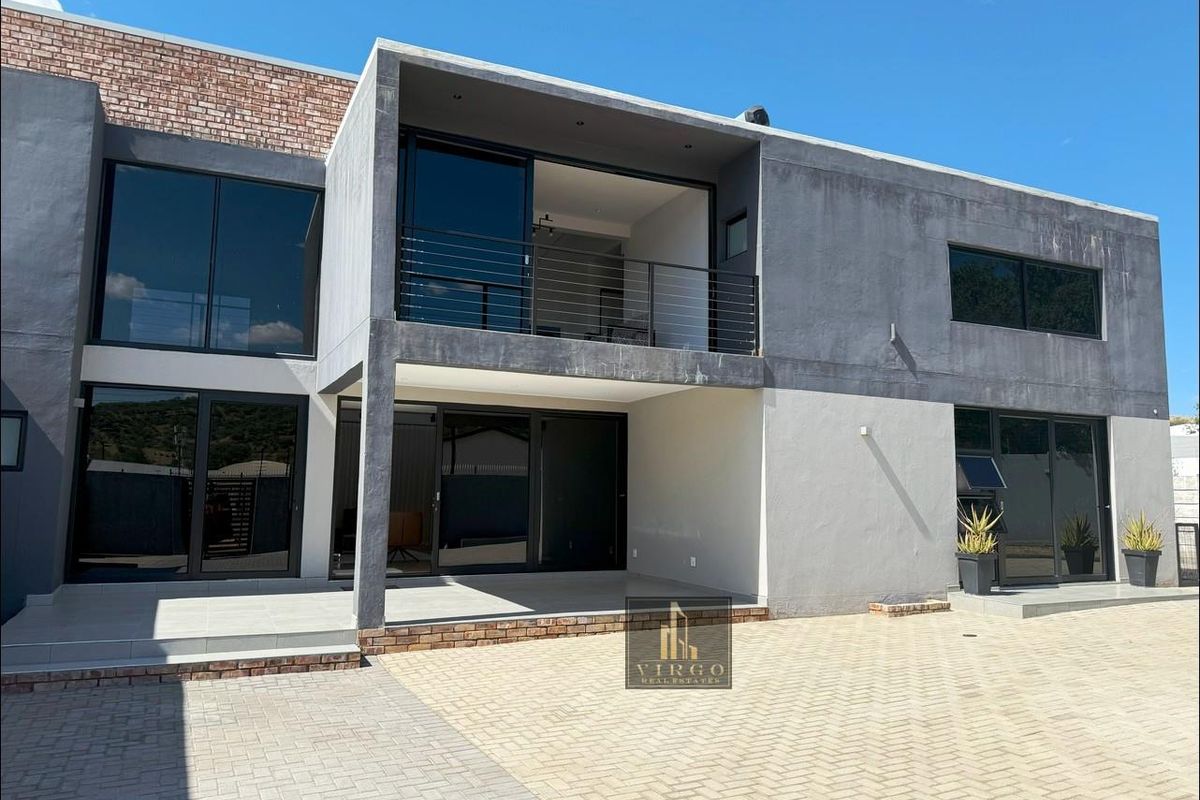 Modern two-story rear elevation featuring large sliding glass doors, a covered patio, and an upper-level balcony with metal railings.
