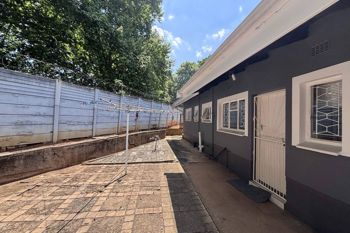 Rear exterior view of the property featuring a paved patio area, secure boundary wall with razor wire, and security gates on the building access points.