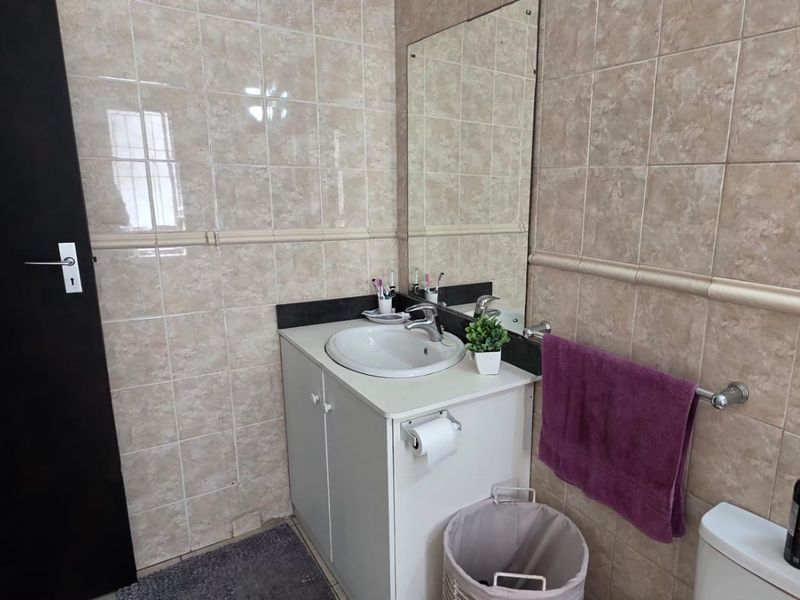 A functional bathroom featuring a vanity cabinet with a basin, wall-mounted mirror, and full-height ceramic wall tiling.
