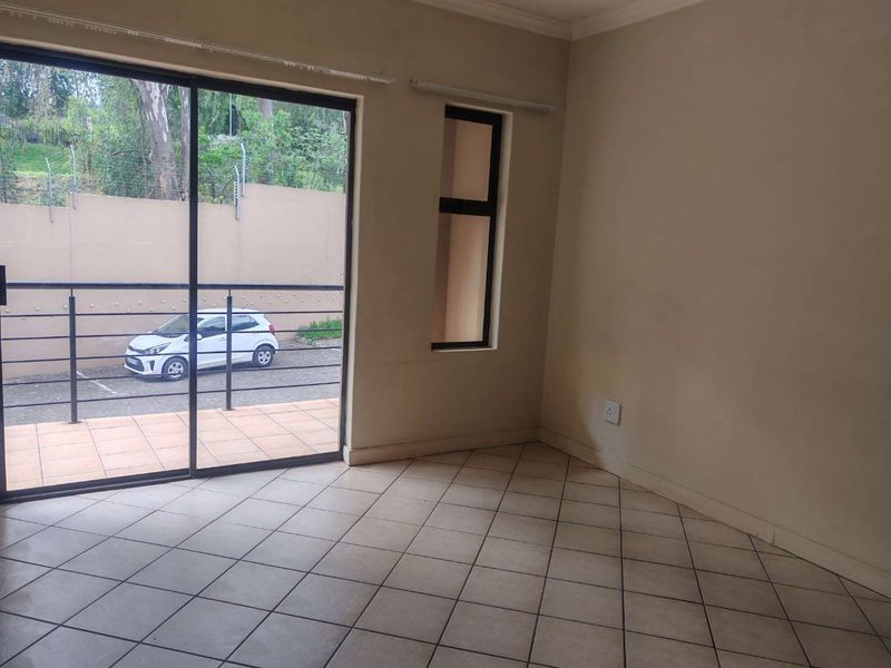 An empty, neutrally painted living area featuring tiled flooring and a large sliding glass door providing access to an outdoor patio space.