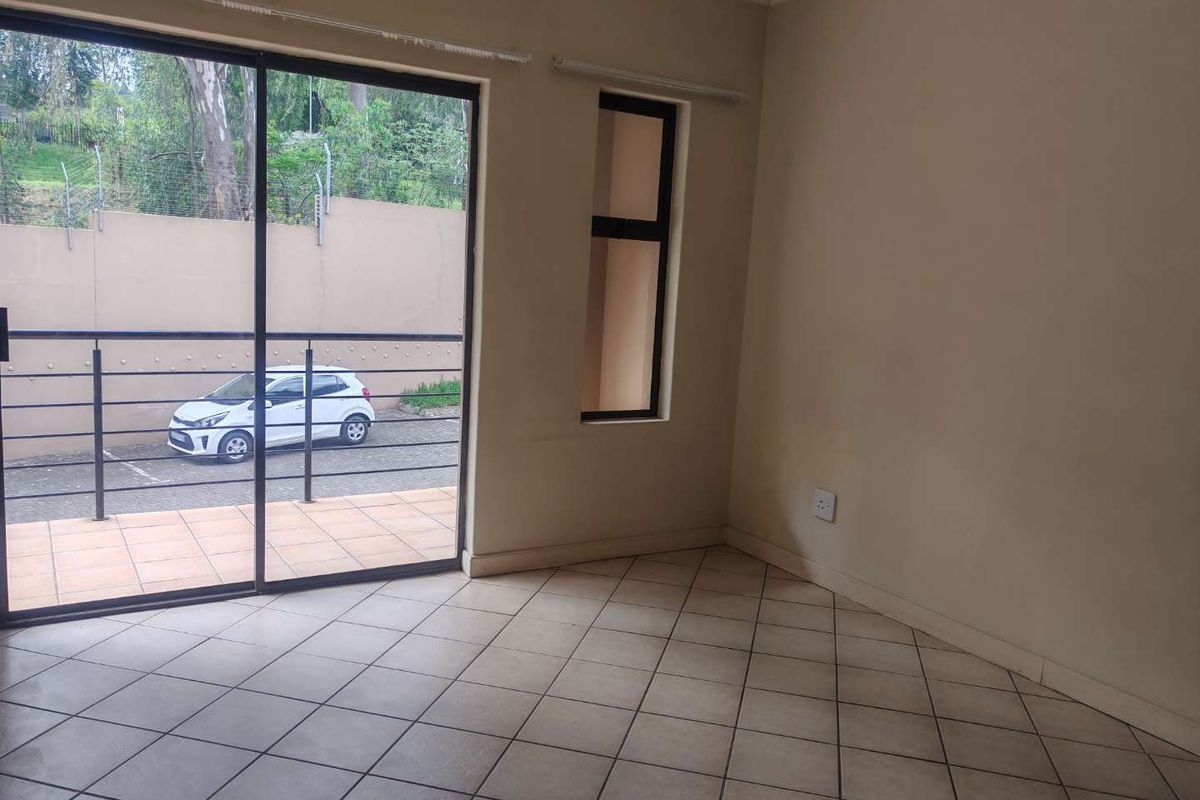 An empty, neutrally painted living area featuring tiled flooring and a large sliding glass door providing access to an outdoor patio space.
