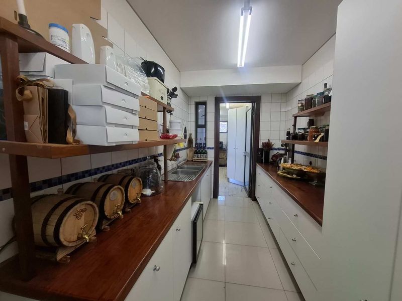 A functional scullery featuring wooden countertops, double bowl sink, ample built-in cabinetry, and tiled finishes throughout.