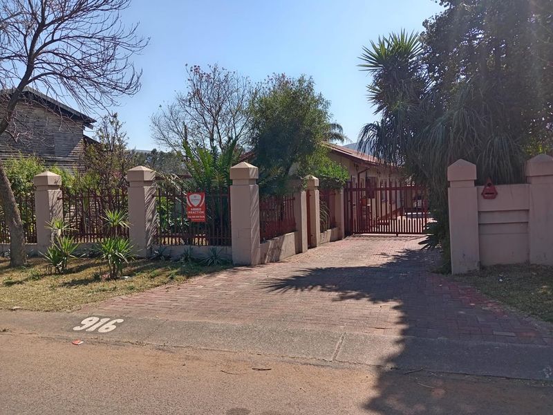 Front view of the property featuring a brick paved driveway, secure perimeter wall with metal fencing, and gated entrance.