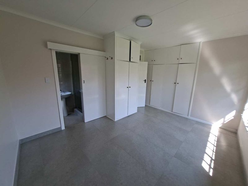A clean, empty bedroom featuring neutral tiled flooring, extensive built-in cupboard storage, and direct access to an en-suite bathroom.