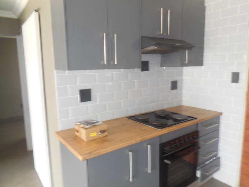 A modern kitchen featuring grey cabinetry, a subway tile backsplash, wood-look countertops, and integrated cooking appliances.