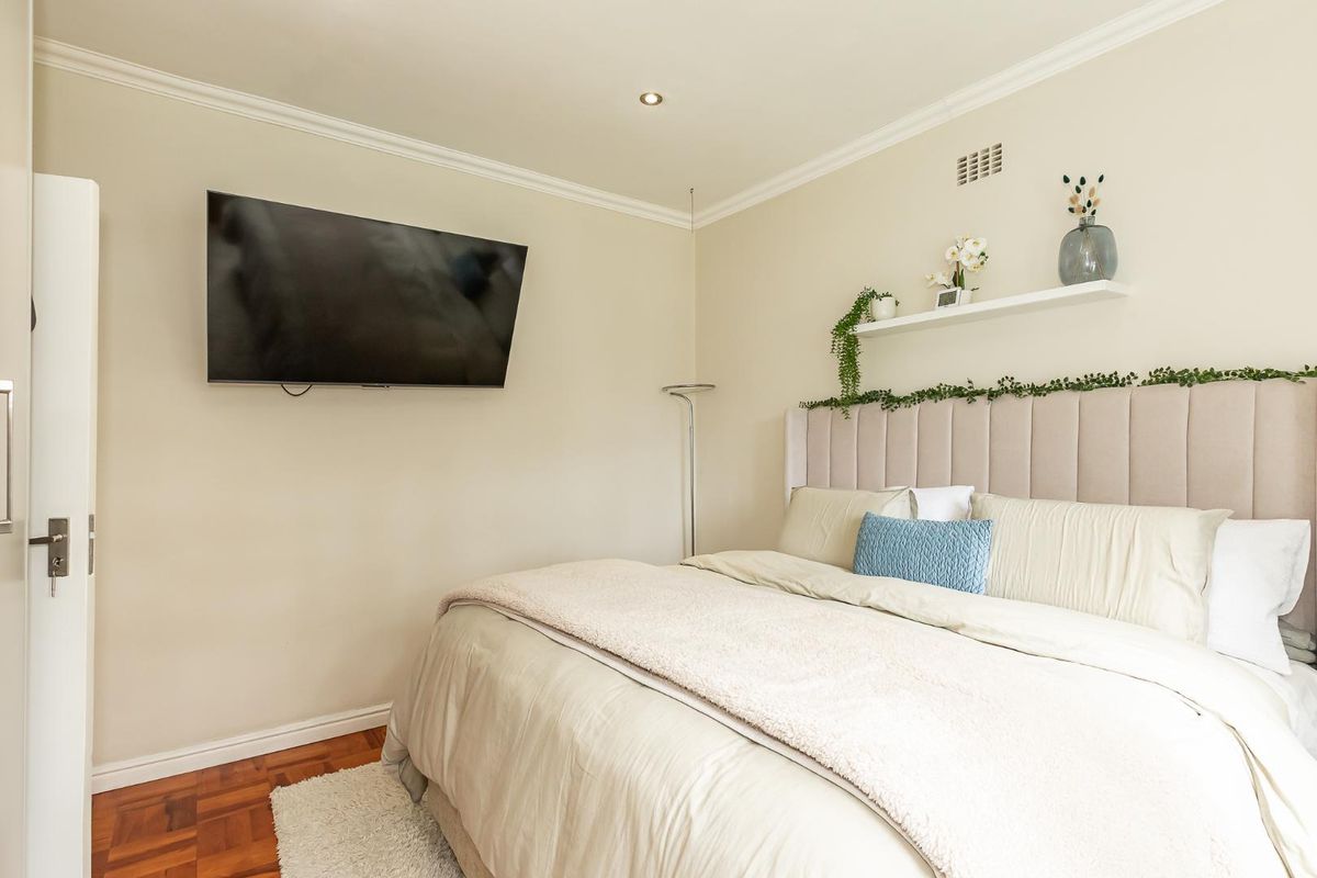 A well-maintained bedroom featuring parquet flooring, crown molding, recessed lighting, and a wall-mounted television.