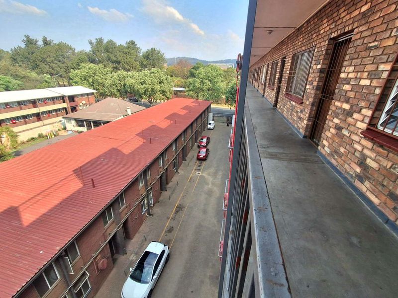 An elevated exterior walkway featuring exposed brick walls, metal security bars, and a concrete floor overlooking the apartment complex grounds.
