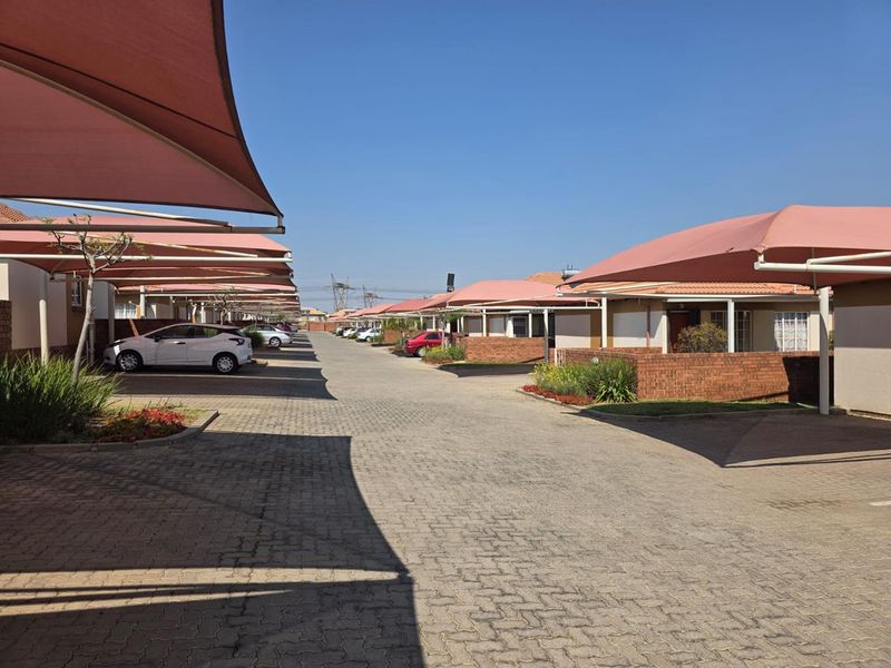 A well-maintained townhouse complex driveway featuring paved surfaces, facebrick boundary walls, and covered shade cloth parking bays for residents.