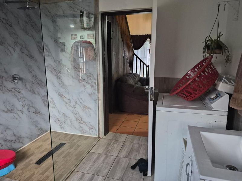 A functional bathroom featuring a modern walk-in shower with marble-look wall cladding, tiled flooring, and an integrated vanity basin.