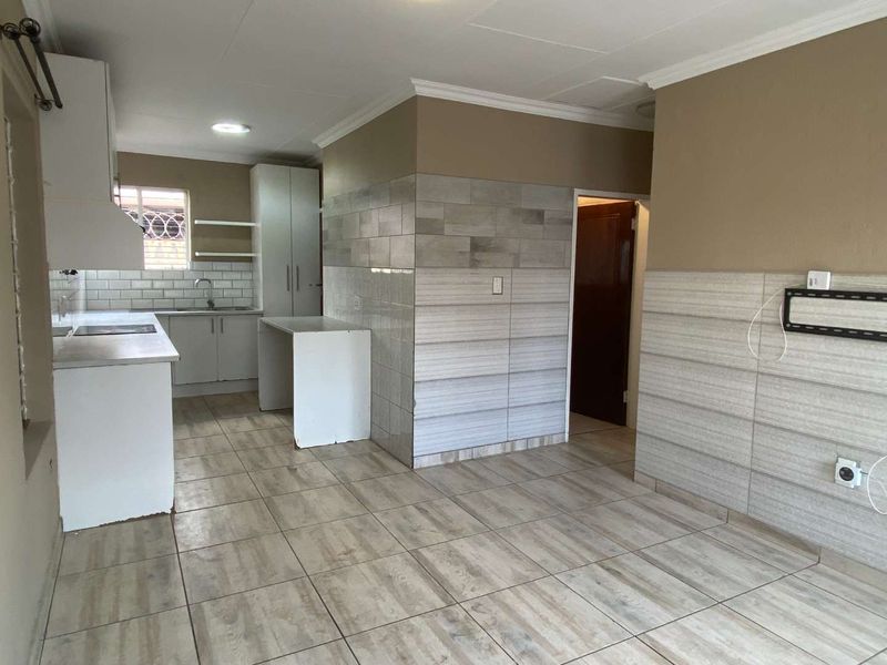 Open-plan kitchen and living area featuring modern tiled flooring, neutral wall finishes, and built-in cabinetry with integrated kitchen fixtures.