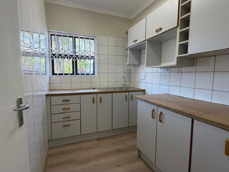 A clean, functional kitchen featuring white cabinetry, wood-look laminate countertops, tiled backsplash, and a stainless steel sink.
