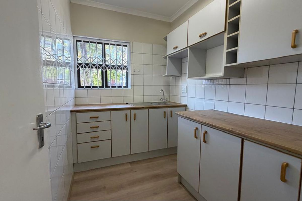 A clean, functional kitchen featuring white cabinetry, wood-look laminate countertops, tiled backsplash, and a stainless steel sink.