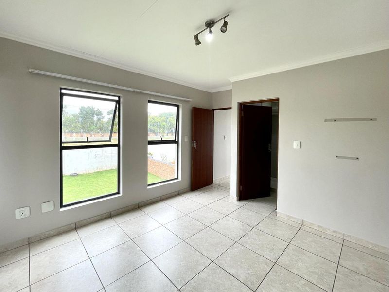 A bright, empty bedroom featuring neutral tiled flooring, large aluminium-framed windows, and clean finishes, ready for personalization.